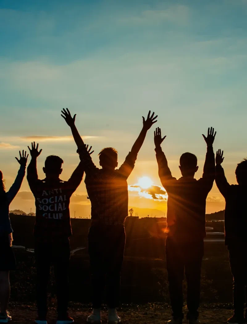 Group of people raising their arms at sunset