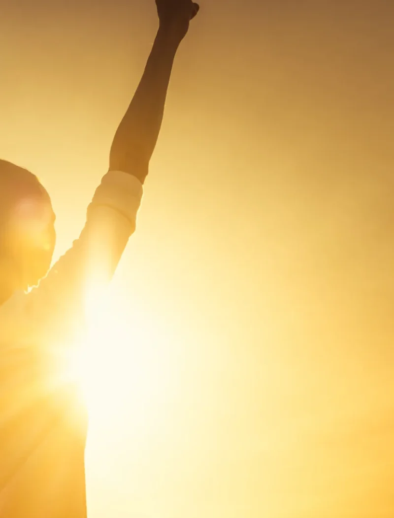 Silhouette of a woman raising her arm toward the sun