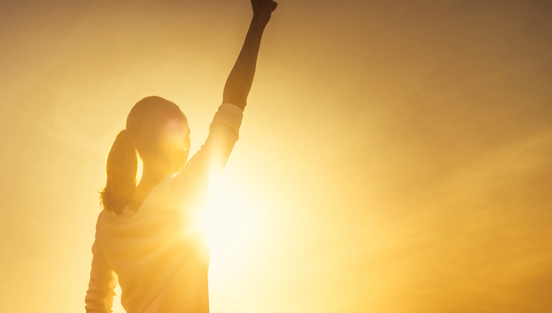 Silhouette of a woman raising her arm toward the sun