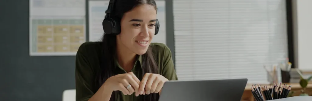 Mujer con audífonos sonriendo frente a su portátil
