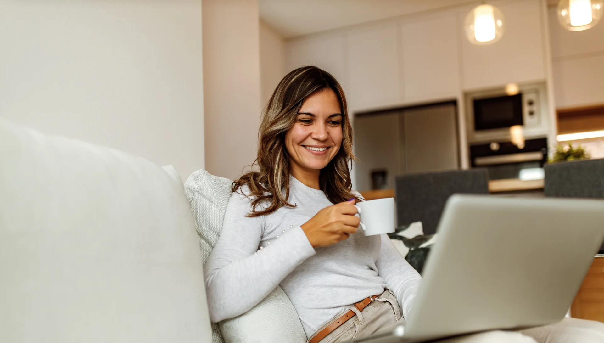 Mujer sonriente con una taza estudiando en su portátil desde casa